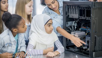 Eine Frau zeigt vier Mädchen das Innere eines Computers