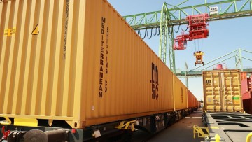 Gelber Container auf Schiene vor Kran