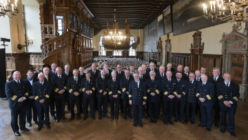 34 Kapitäne und Kapitäninnen stehen in Uniform aufgereicht in einem großen Saal und lächeln in die Kamera