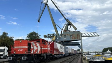 Güterzug neben Kran auf Gleisen neben Binnenschiffen