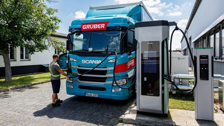 Sieben Geschäftsleute stehen lächelnd vor einem E-Lkw, der vor einem Siemens-Gebäude im Sonnenschein geparkt ist