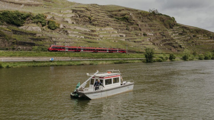 Ein kleines Schiff vor steilen Moselhängen.