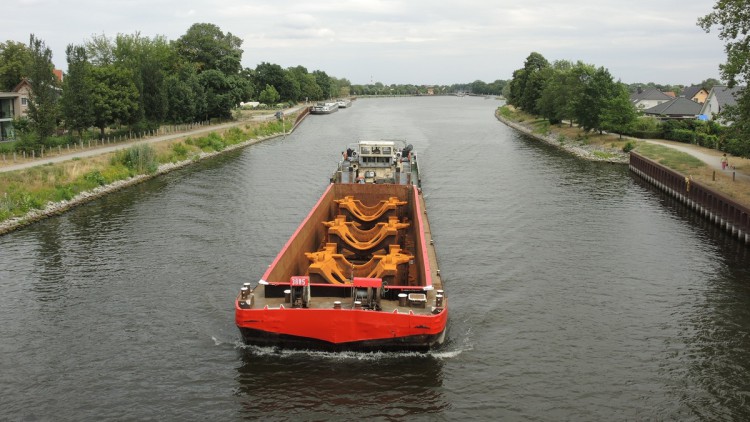 Blick von einer Brücke auf einen Binnenschiff mit rostroten Gussteilen im offenen Laderaum