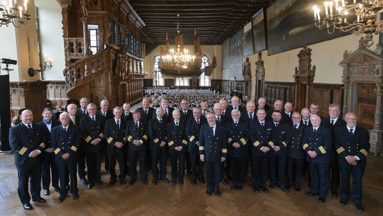 34 Kapitäne und Kapitäninnen stehen in Uniform aufgereicht in einem großen Saal und lächeln in die Kamera